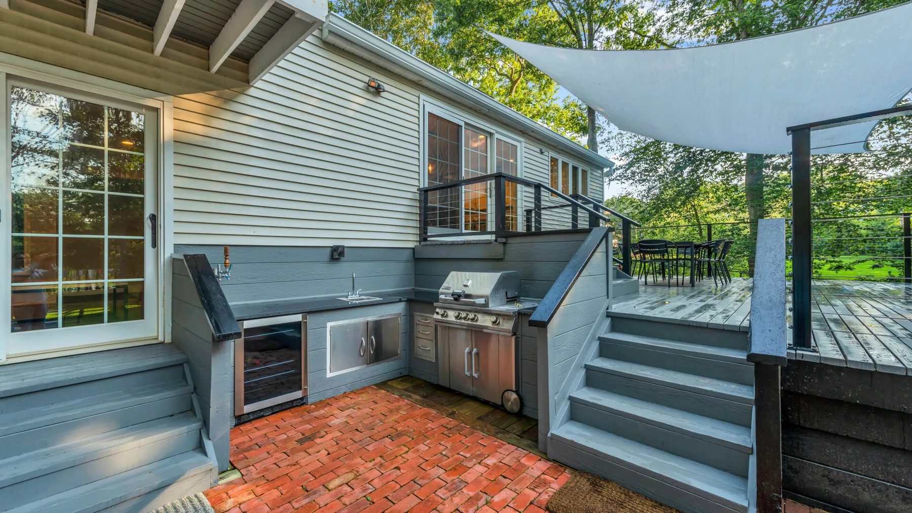 An outdoor deck with a built-in grill and stairs beneath a shade canopy.