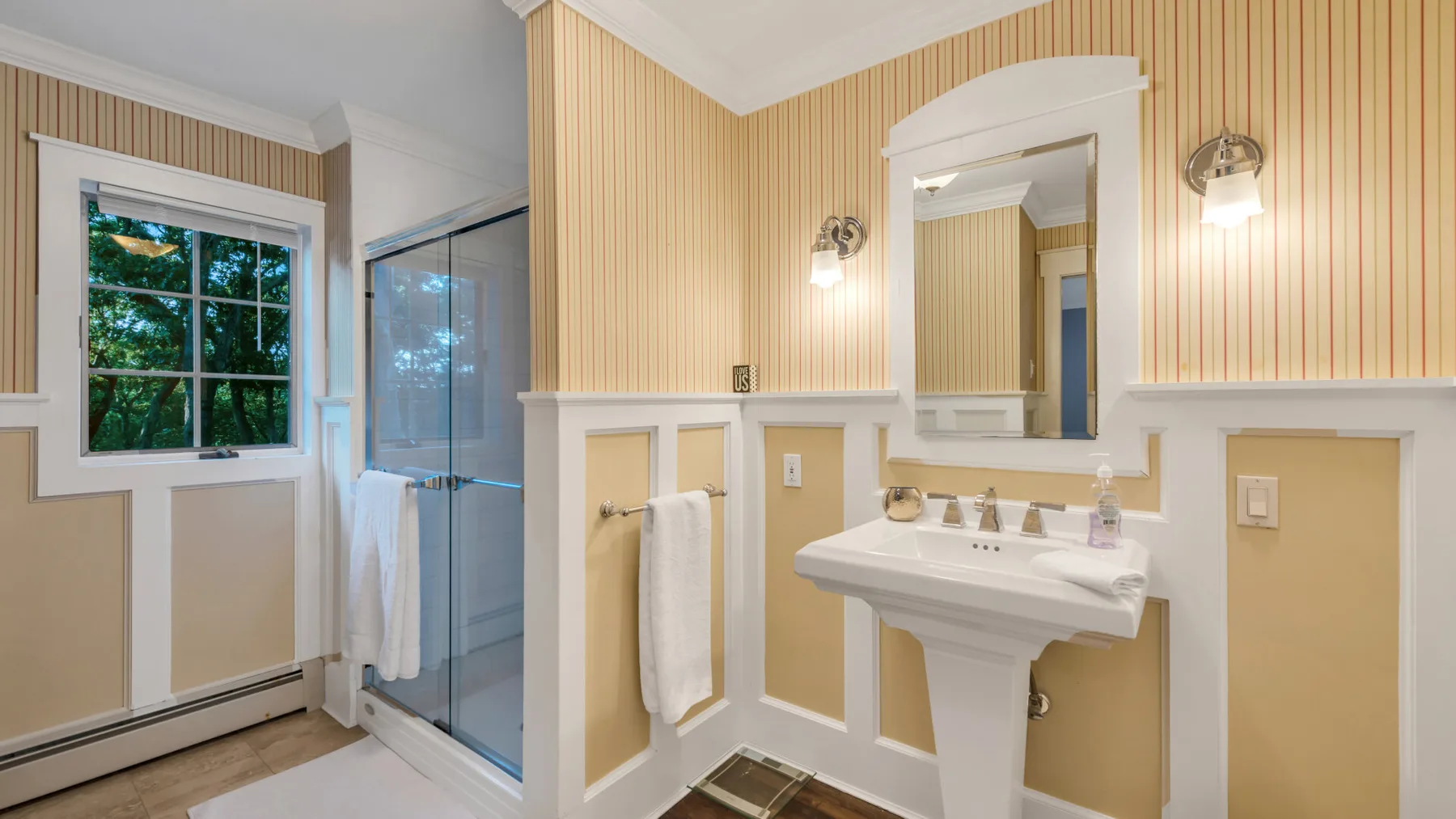 A bright bathroom with a pedestal sink, mirror, and glass shower.