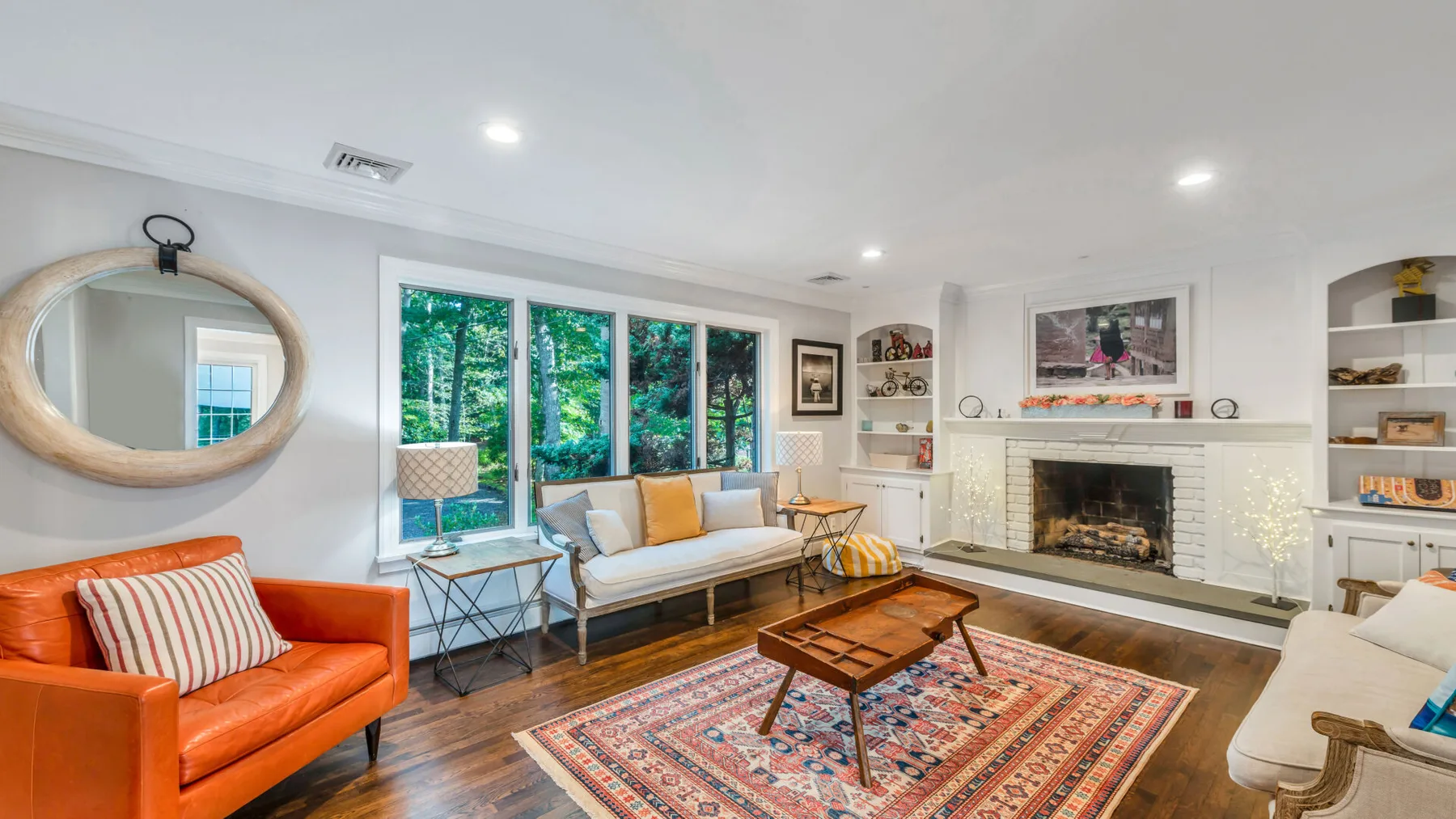 A bright living room with seating, a fireplace, and large windows overlooking greenery.