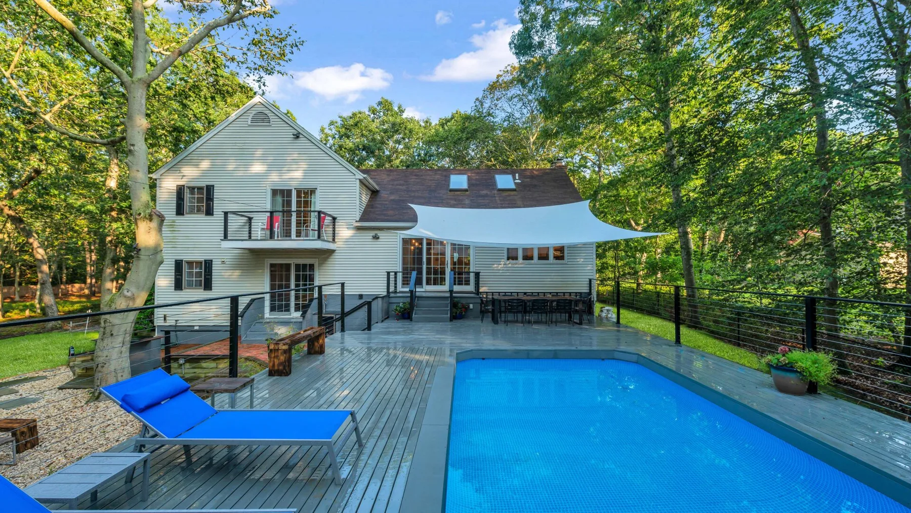 A swimming pool sits beside a spacious wooden deck surrounded by trees.