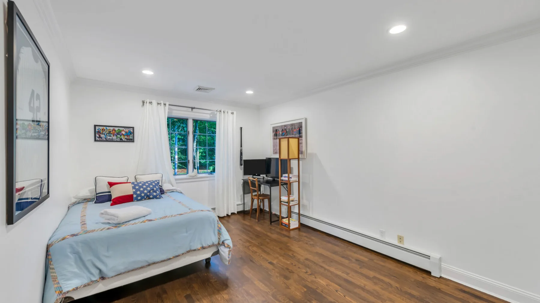 A bright bedroom with a bed, a small desk, and a window.