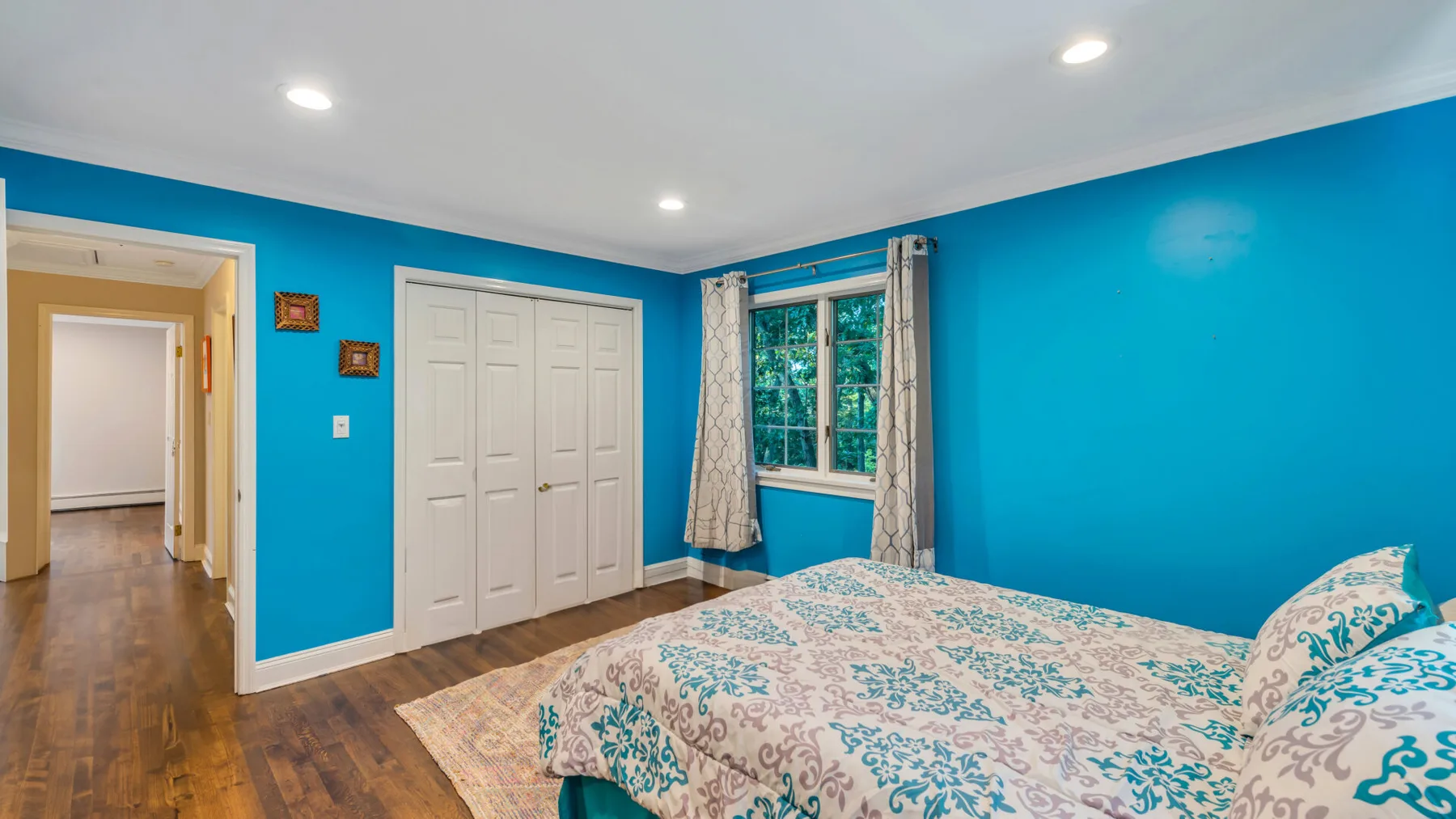 A bedroom with a patterned bed, white closet doors, and a window.