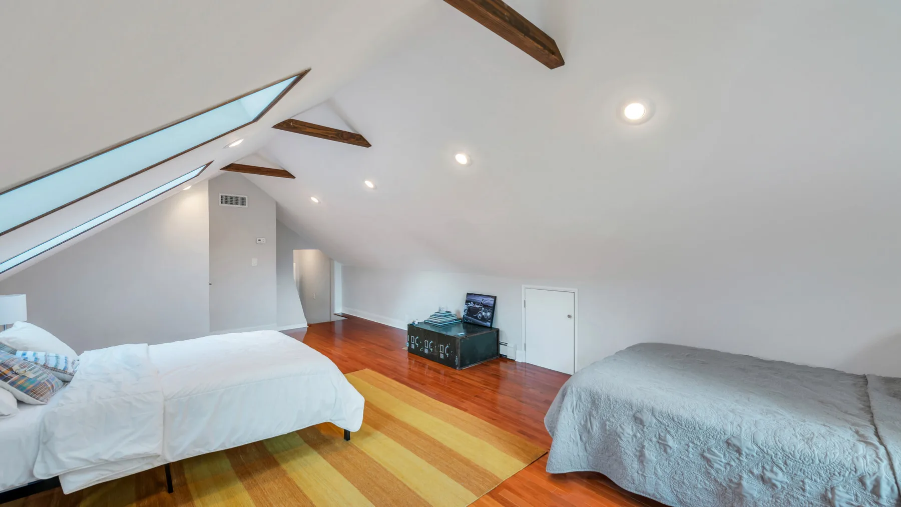 A bedroom with two beds and a low cabinet beneath a sloped ceiling.