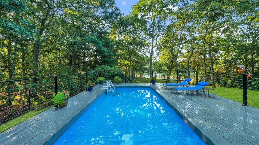 An outdoor swimming pool is surrounded by a wooden deck, seating, and trees.