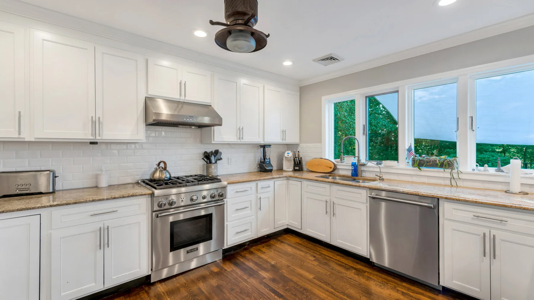 A bright kitchen with white cabinetry, stainless steel appliances, and large windows.