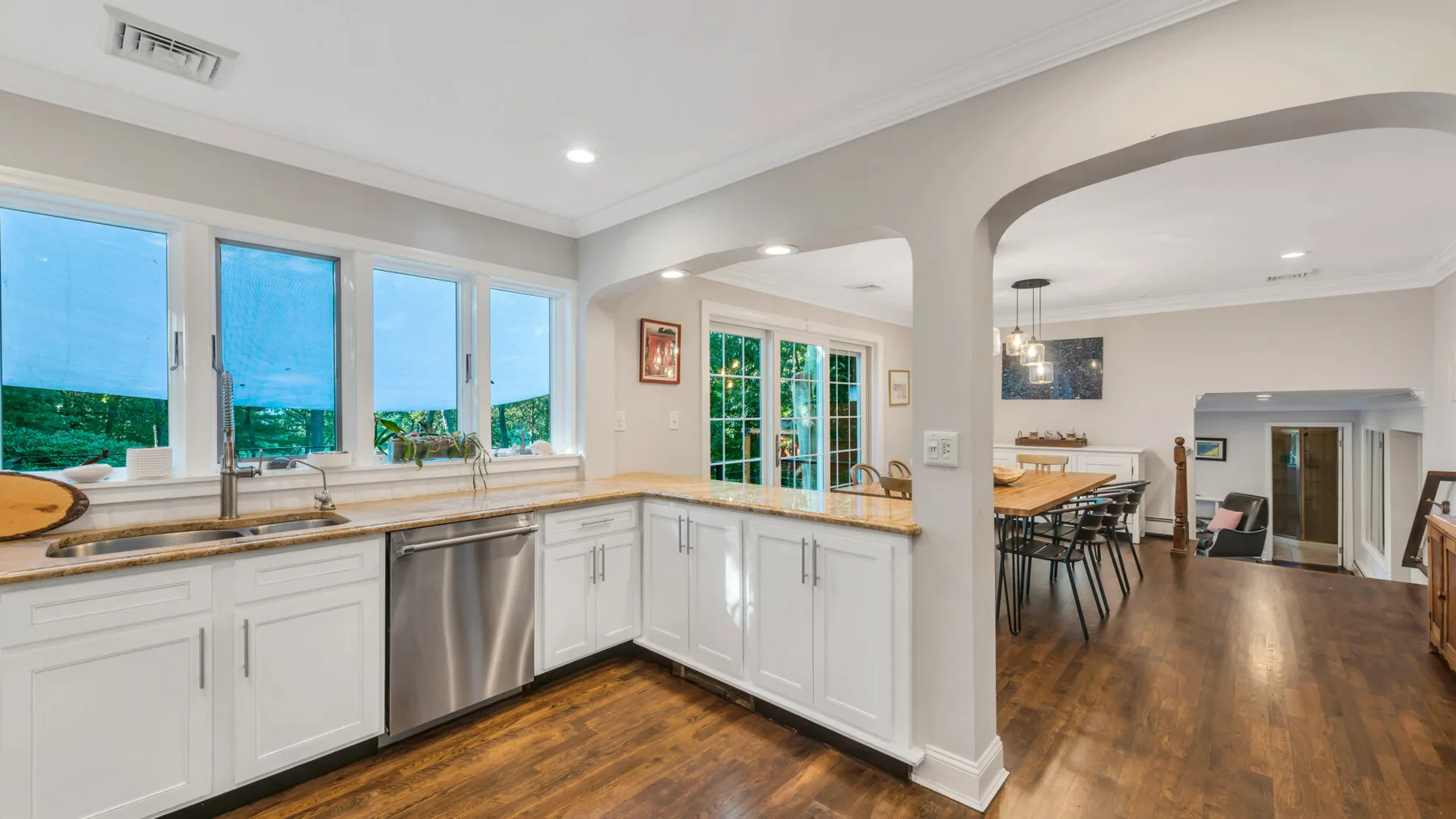 A bright kitchen with white cabinetry and a dining area beyond the arched opening.