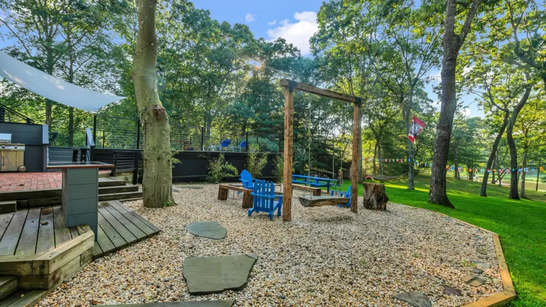 A wooded outdoor seating area with wooden benches and a gravel ground.
