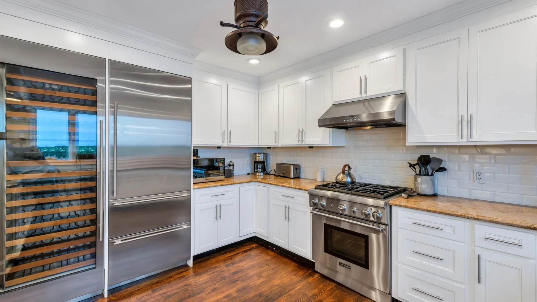 A bright kitchen with white cabinets, stainless steel appliances, and a wood floor.