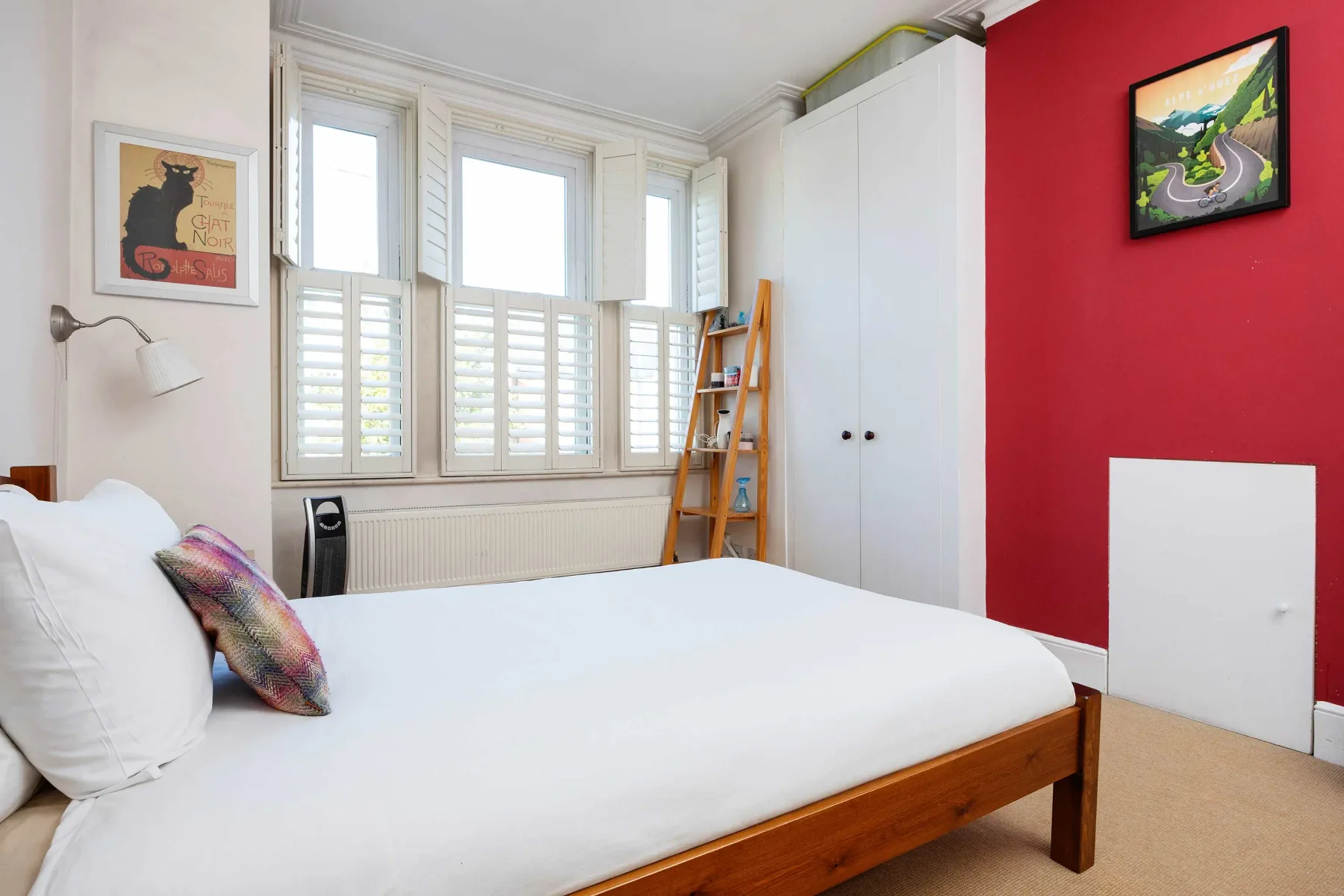 Un dormitorio con una cama, ventanas altas y una pared roja.