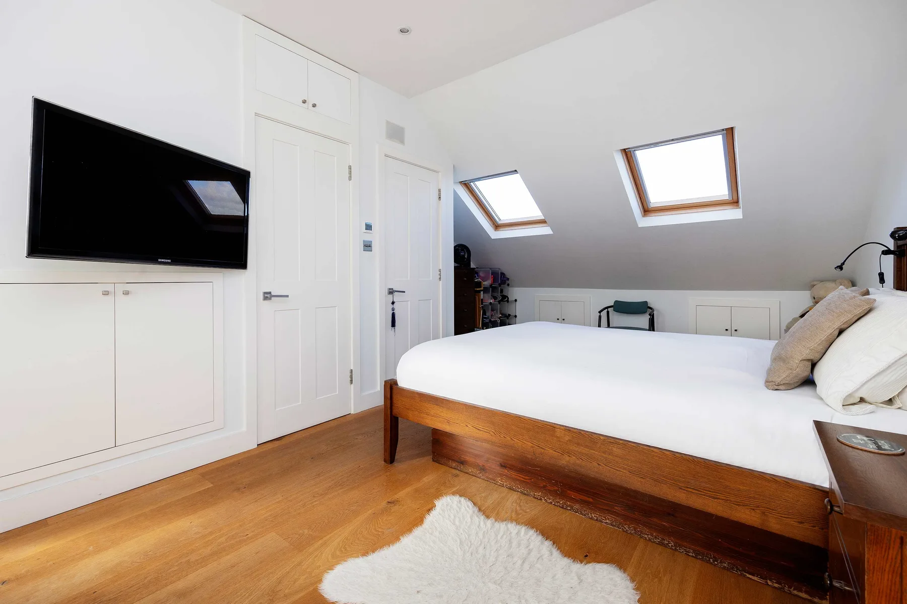 Un dormitorio luminoso con una cama de madera, ropa de cama blanca y tragaluces.