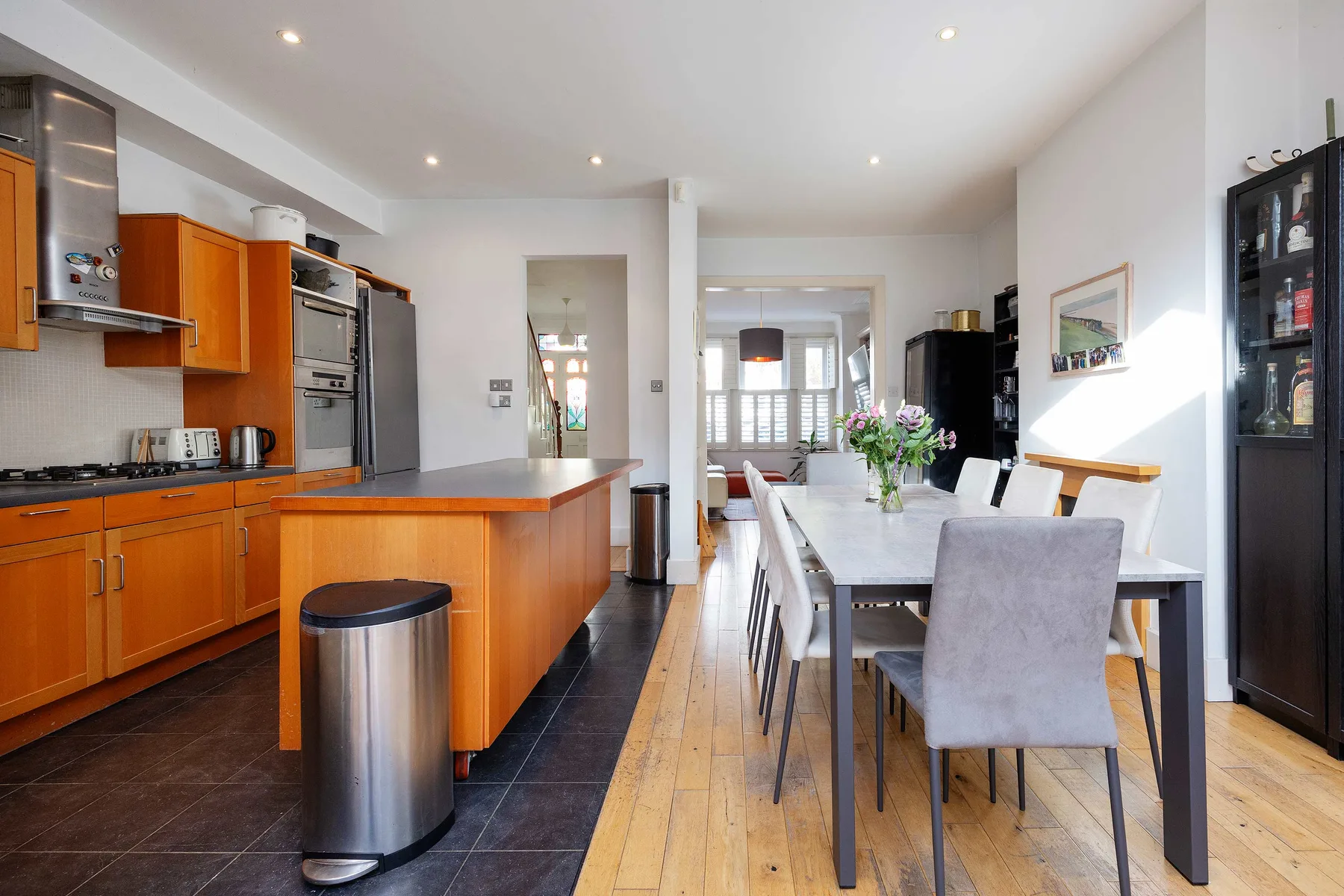 Cocina abierta y comedor con armarios de madera y una mesa larga.