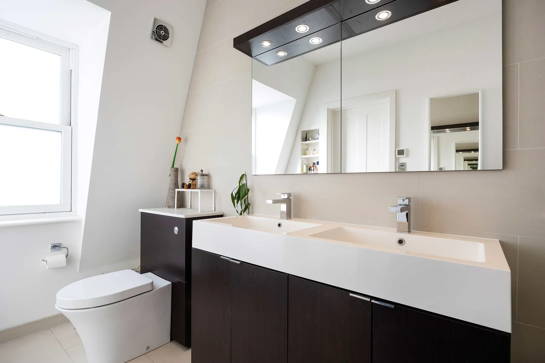 Un baño luminoso con un tocador largo, un espejo amplio y un inodoro junto a una ventana.