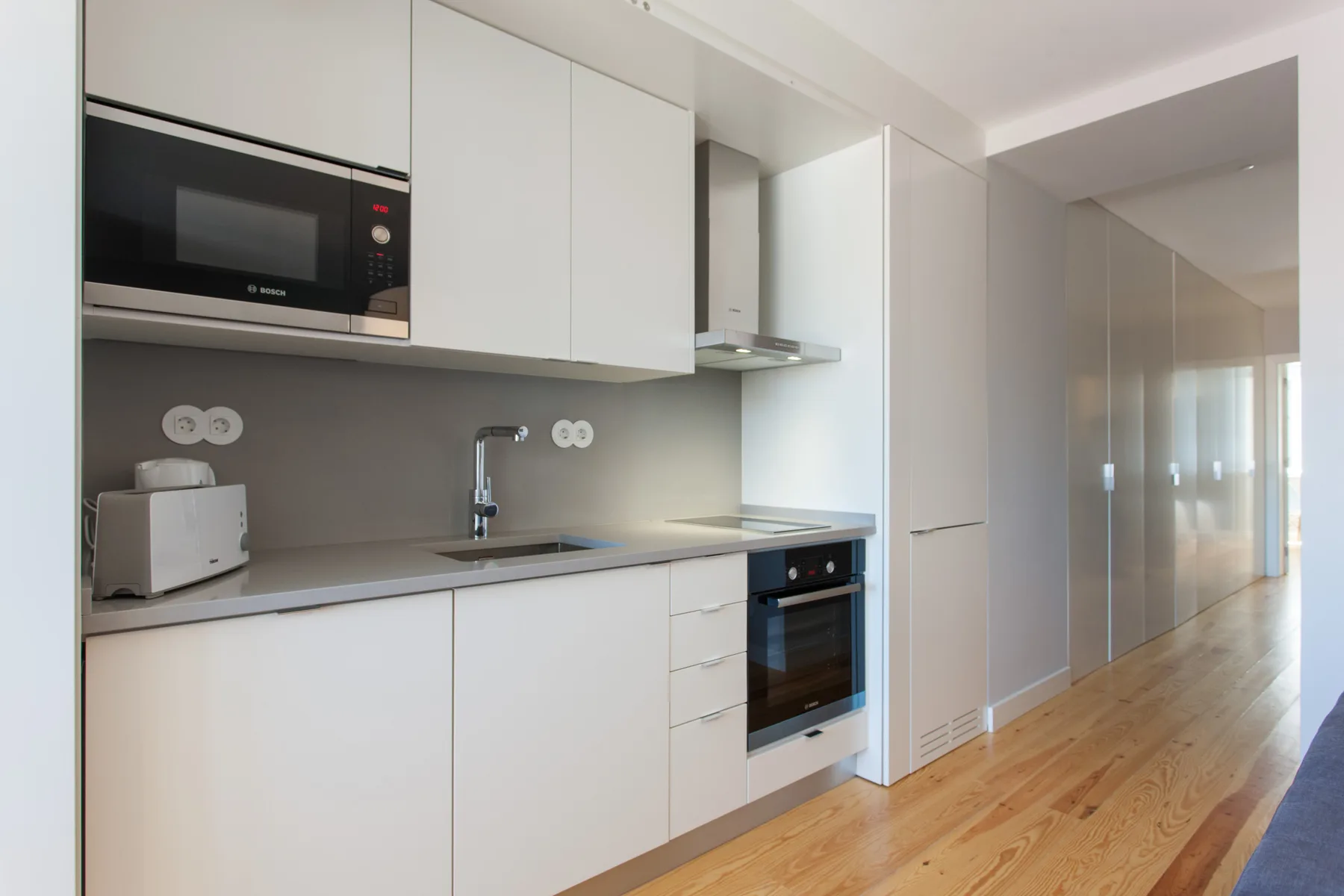 Una cocina moderna con armarios blancos, una encimera y suelo de madera.