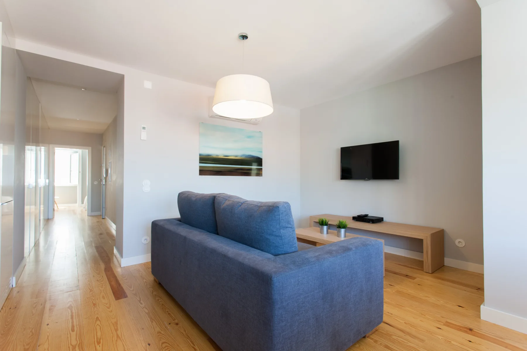 Sala de estar con asientos azules, un televisor en la pared y una mesa baja de madera.