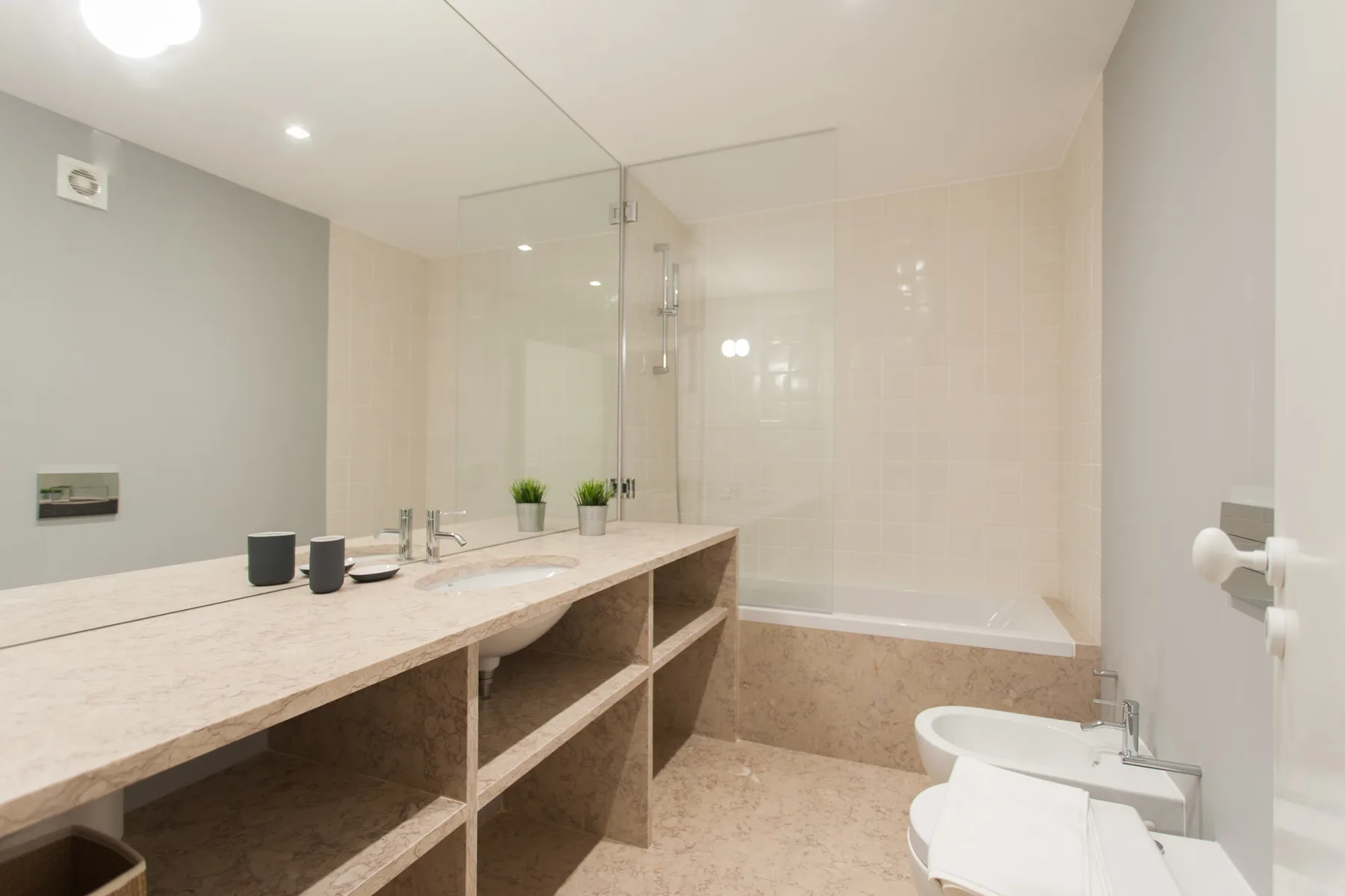 Un baño luminoso con un lavabo largo y una bañera detrás de una mampara de vidrio.