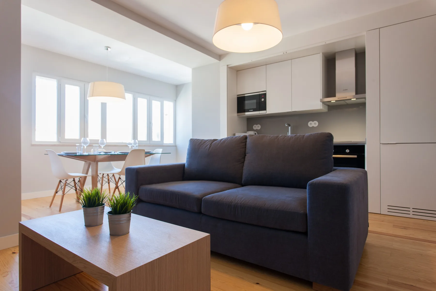 Una sala de estar con asientos oscuros, una mesa de centro y una cocina abierta.