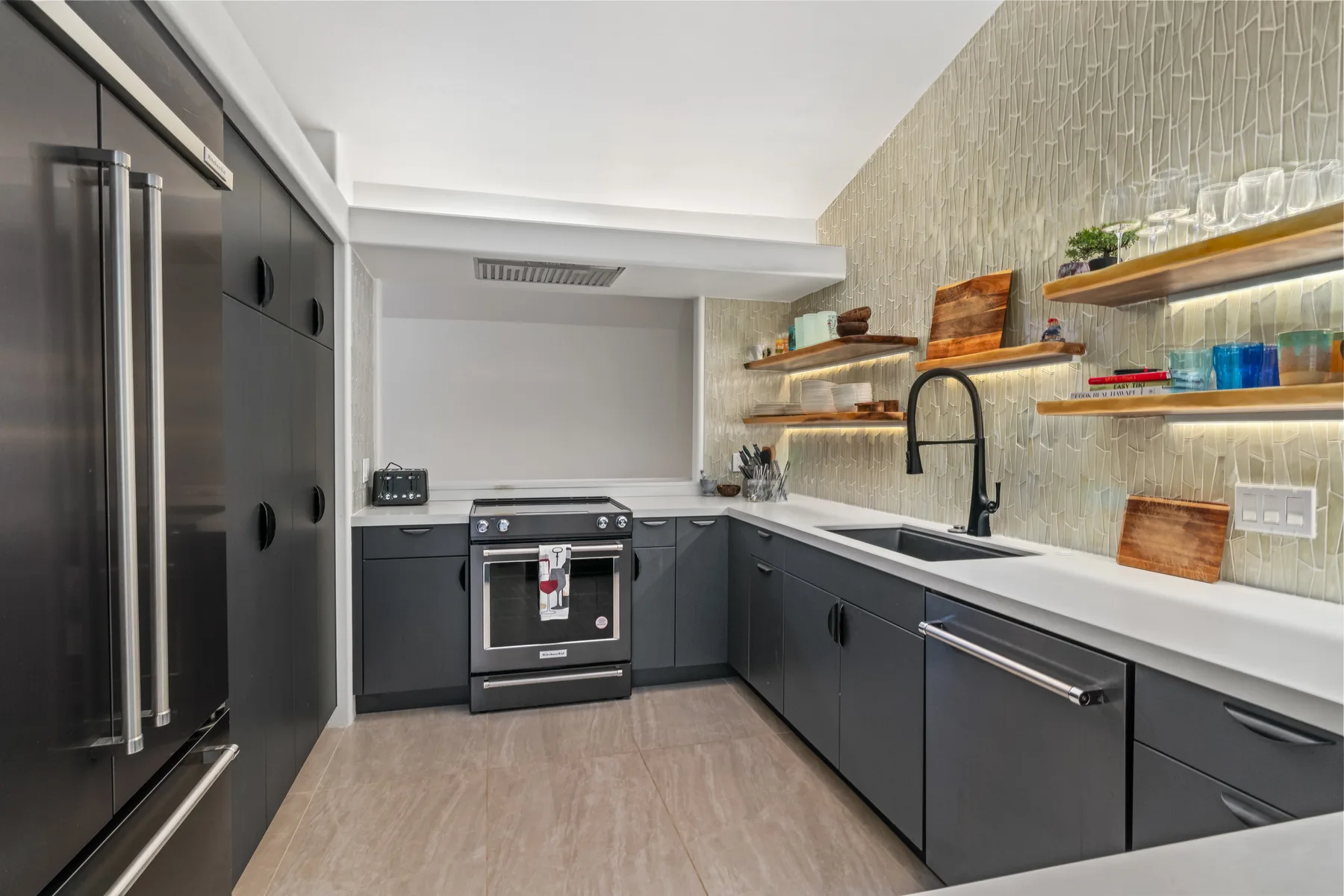 A modern kitchen with dark cabinets, stainless steel appliances, and open shelves.