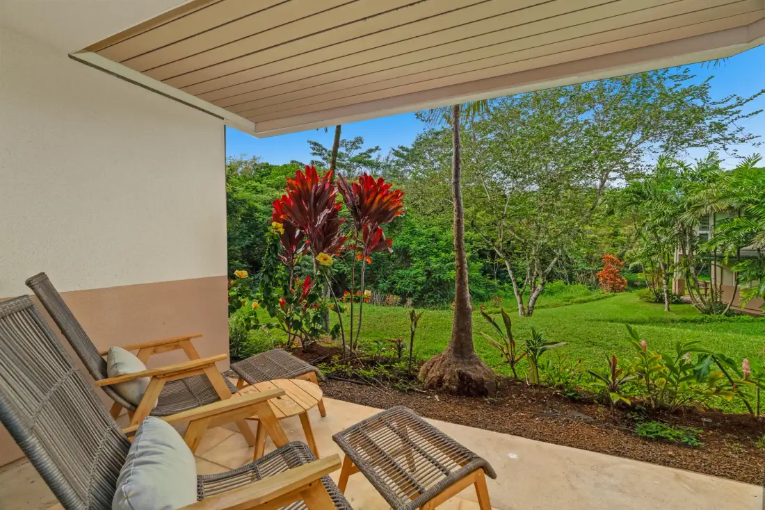 A covered patio with lounge seating overlooks a green garden.