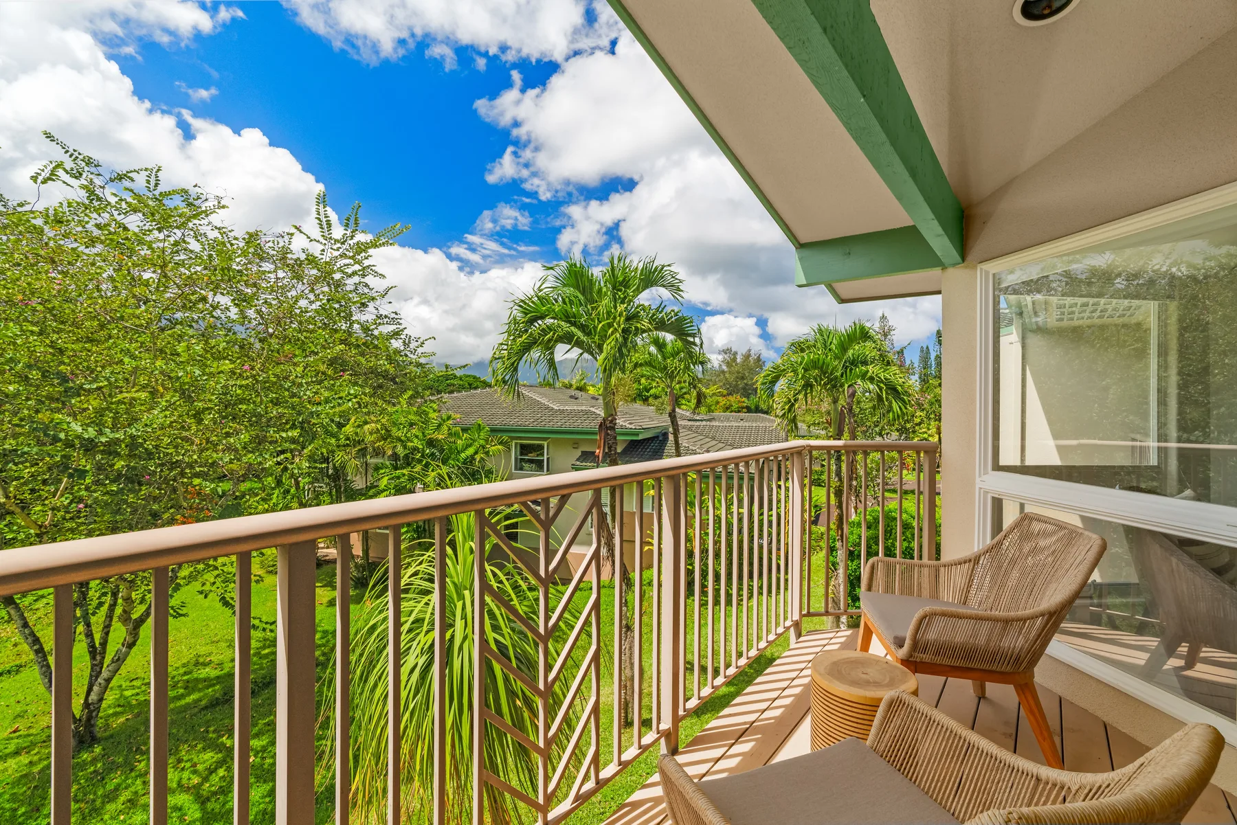 A covered balcony with seating overlooks green trees and nearby homes.