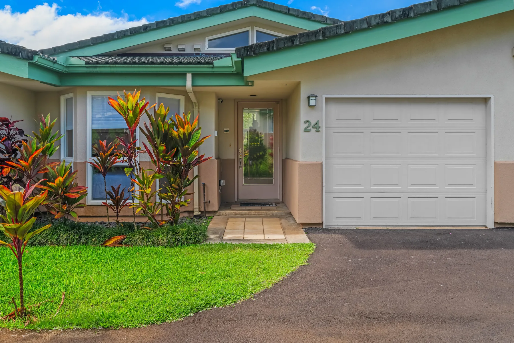A house entrance with a garage, front lawn, and tropical plants.