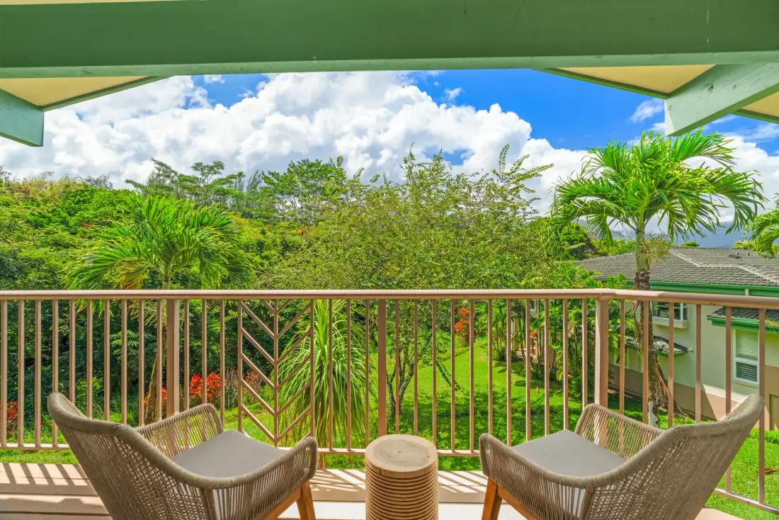 A covered balcony with seating overlooks lush tropical greenery.