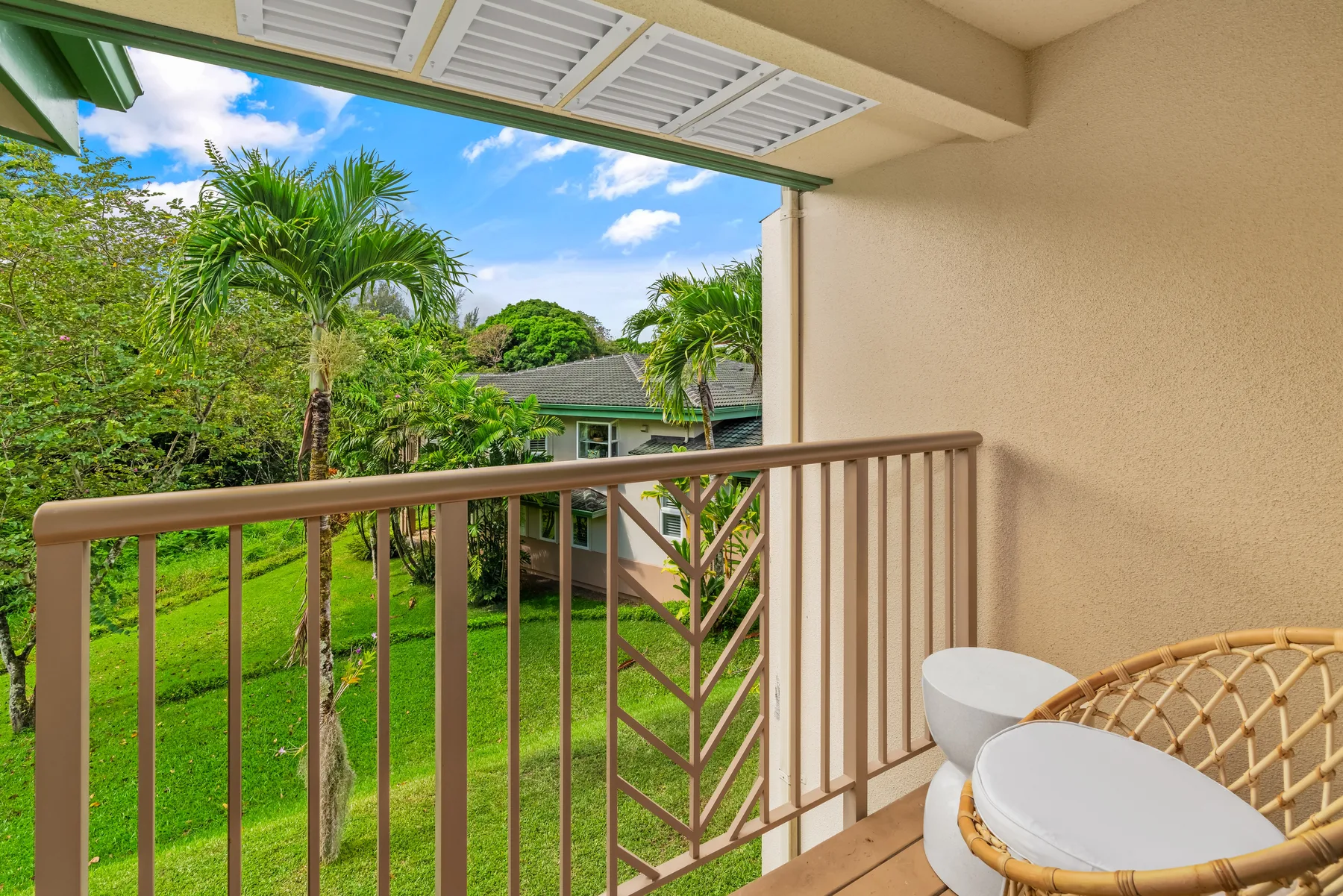 A covered balcony overlooks a green lawn and palm trees.