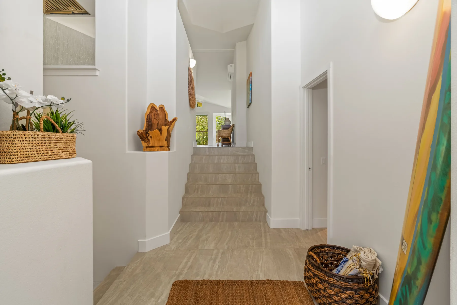 A bright hallway with stairs leading to a window and a basket on the floor.