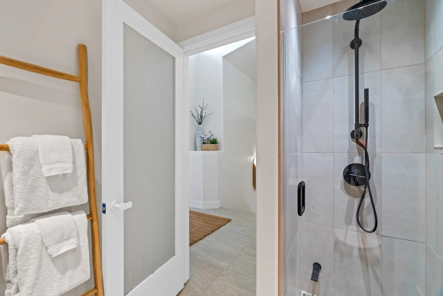 A bathroom shower beside an open doorway, with towels on a wooden rack.