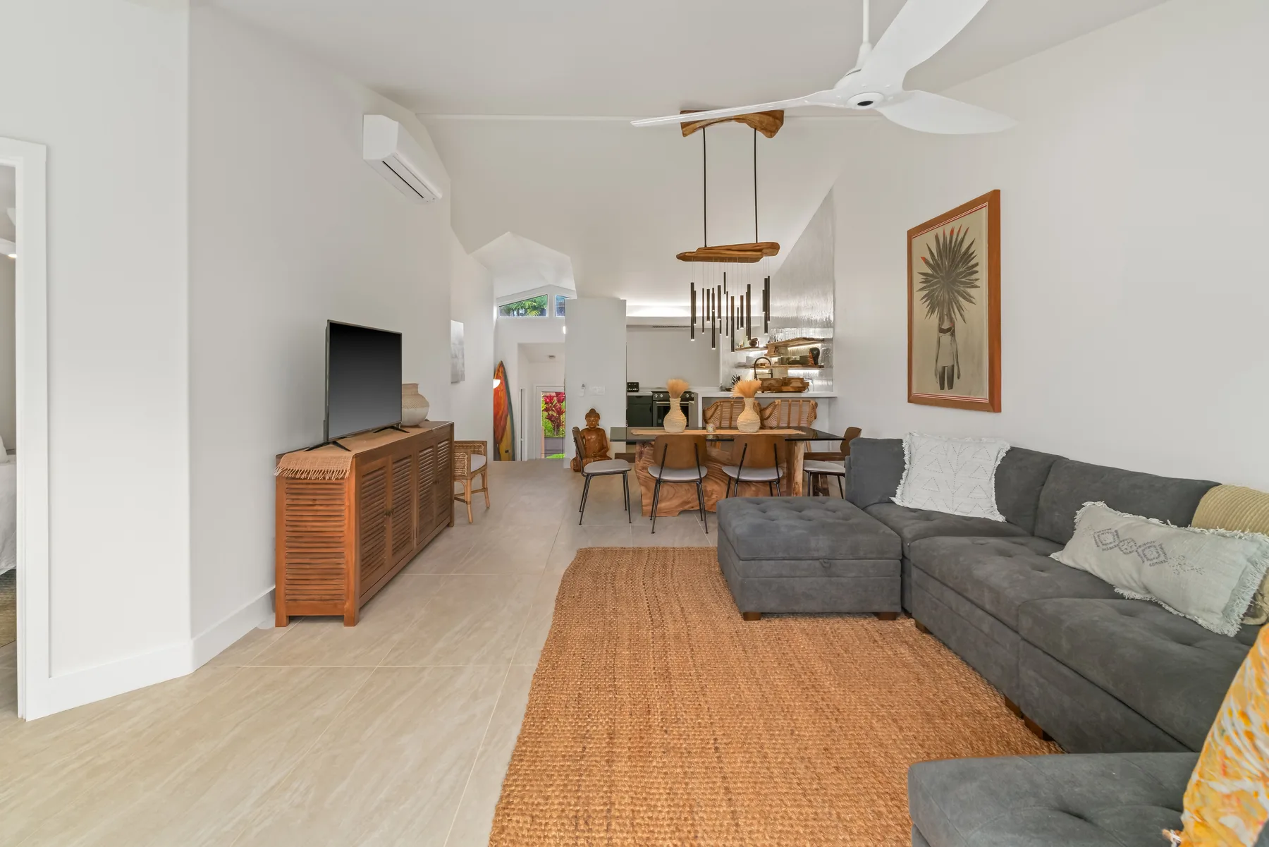 A bright living and dining area with a gray sectional and a wooden dining table.