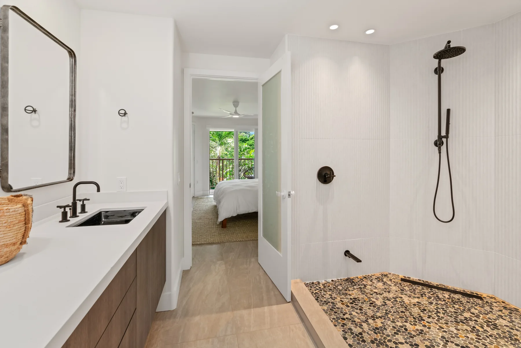 A bathroom with a vanity and an open shower area beside a bedroom doorway.