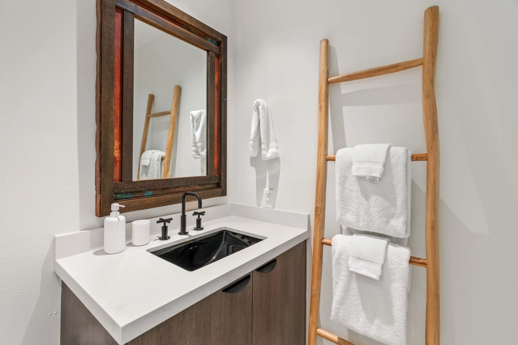 A bathroom vanity with a black sink and a wooden towel ladder.