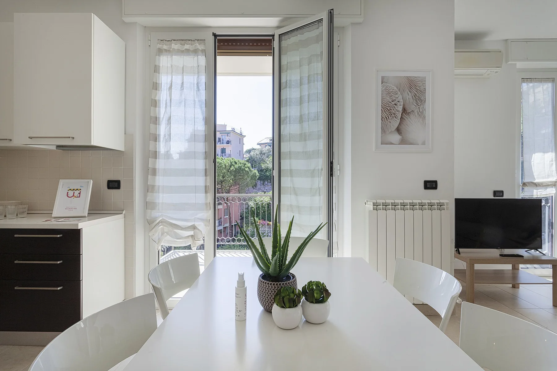 Un comedor luminoso con una mesa blanca y la puerta del balcón abierta.