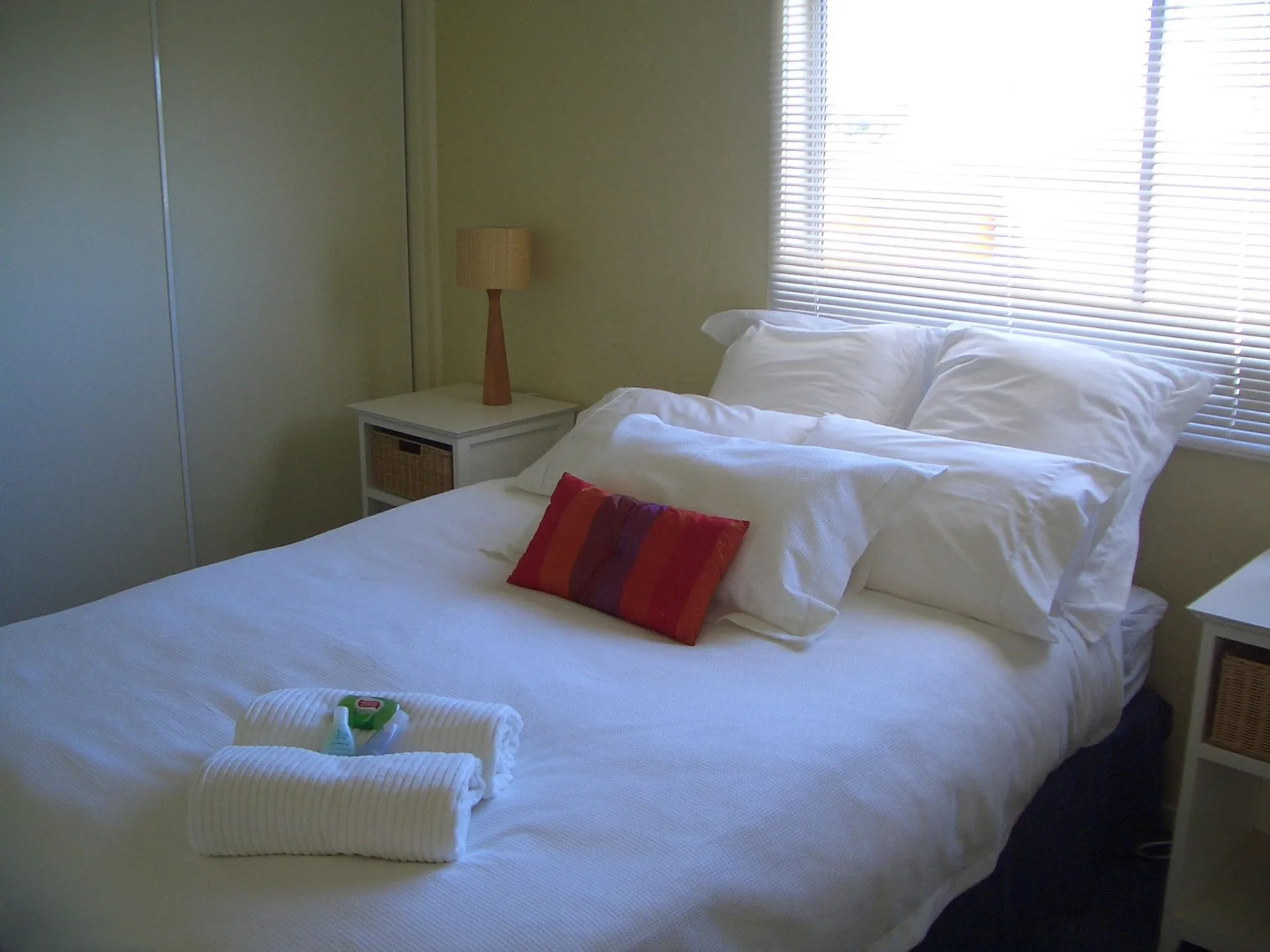 A bedroom with white bedding and a red accent pillow.