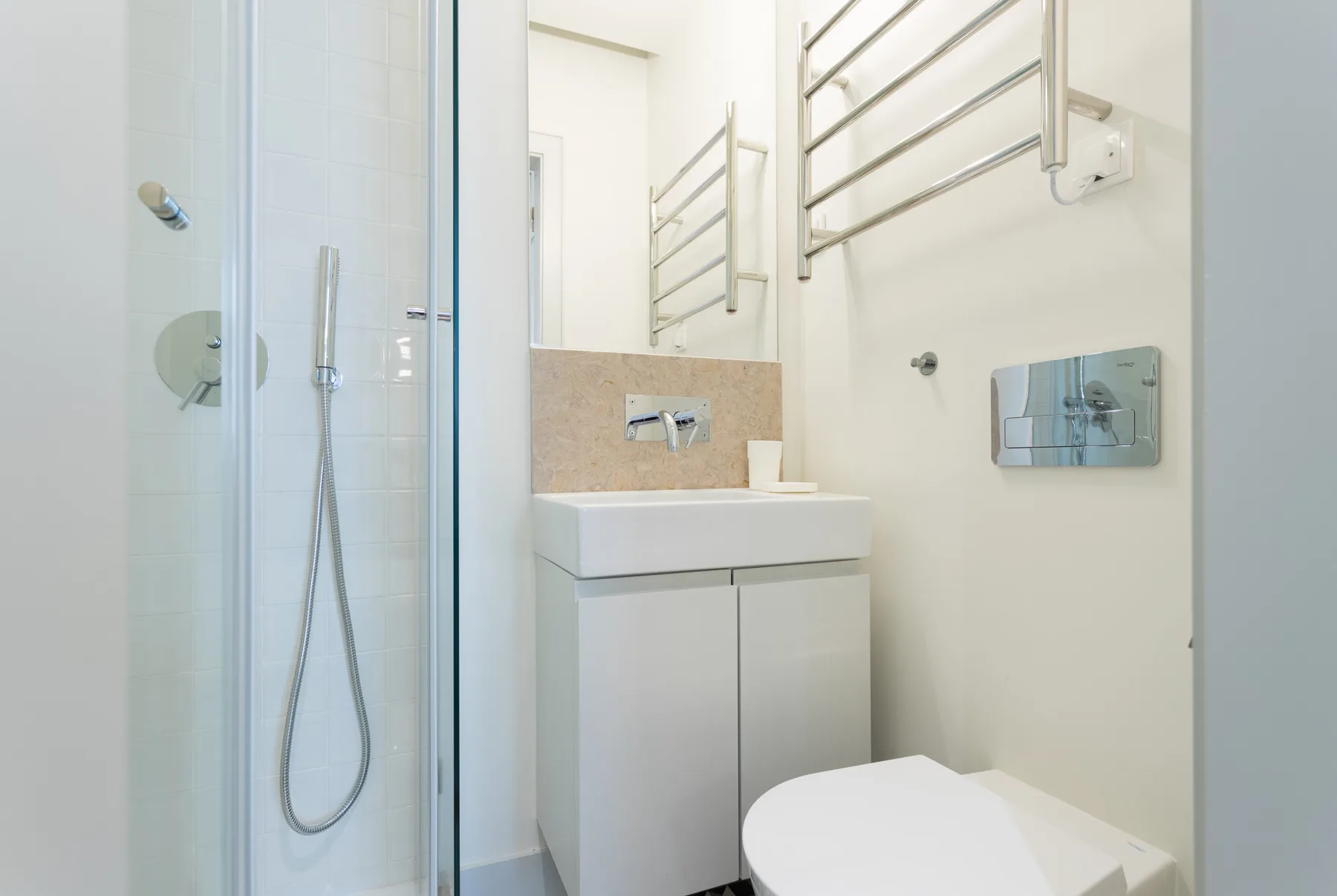 Un baño luminoso con ducha de vidrio, lavabo y toalleros en la pared.