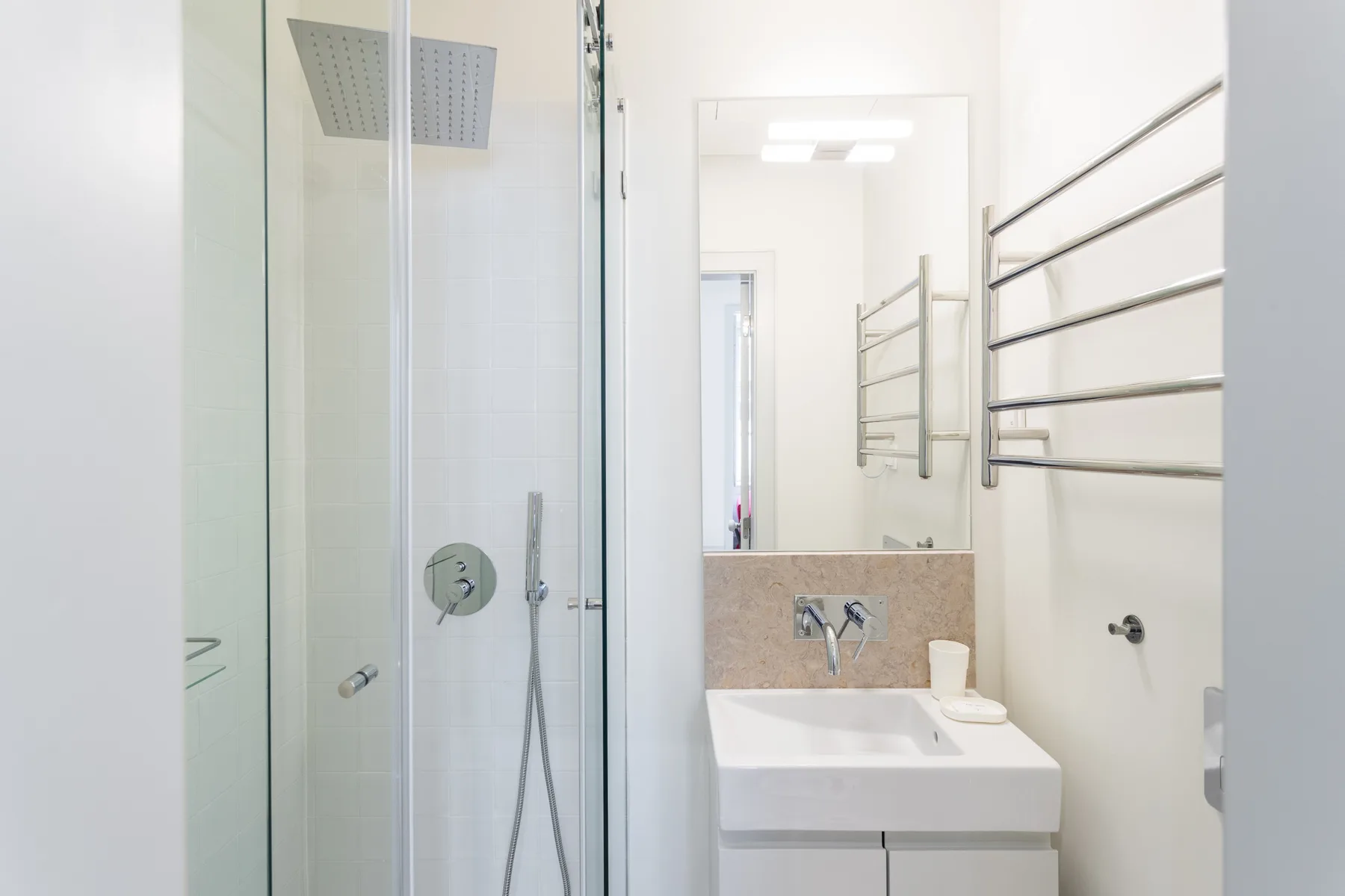 A bright bathroom with a glass shower and a white sink beneath a mirror.