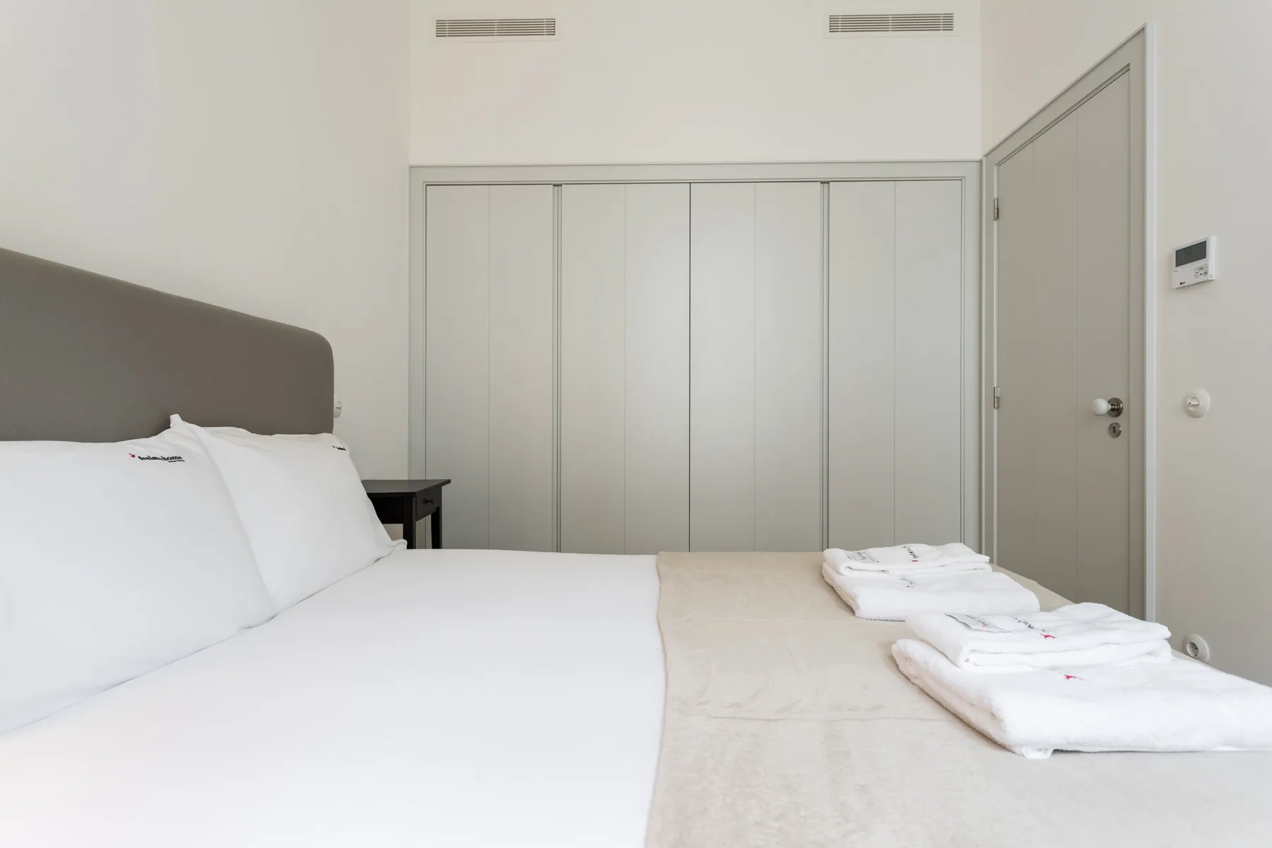 A bedroom with a neatly made bed and folded towels.