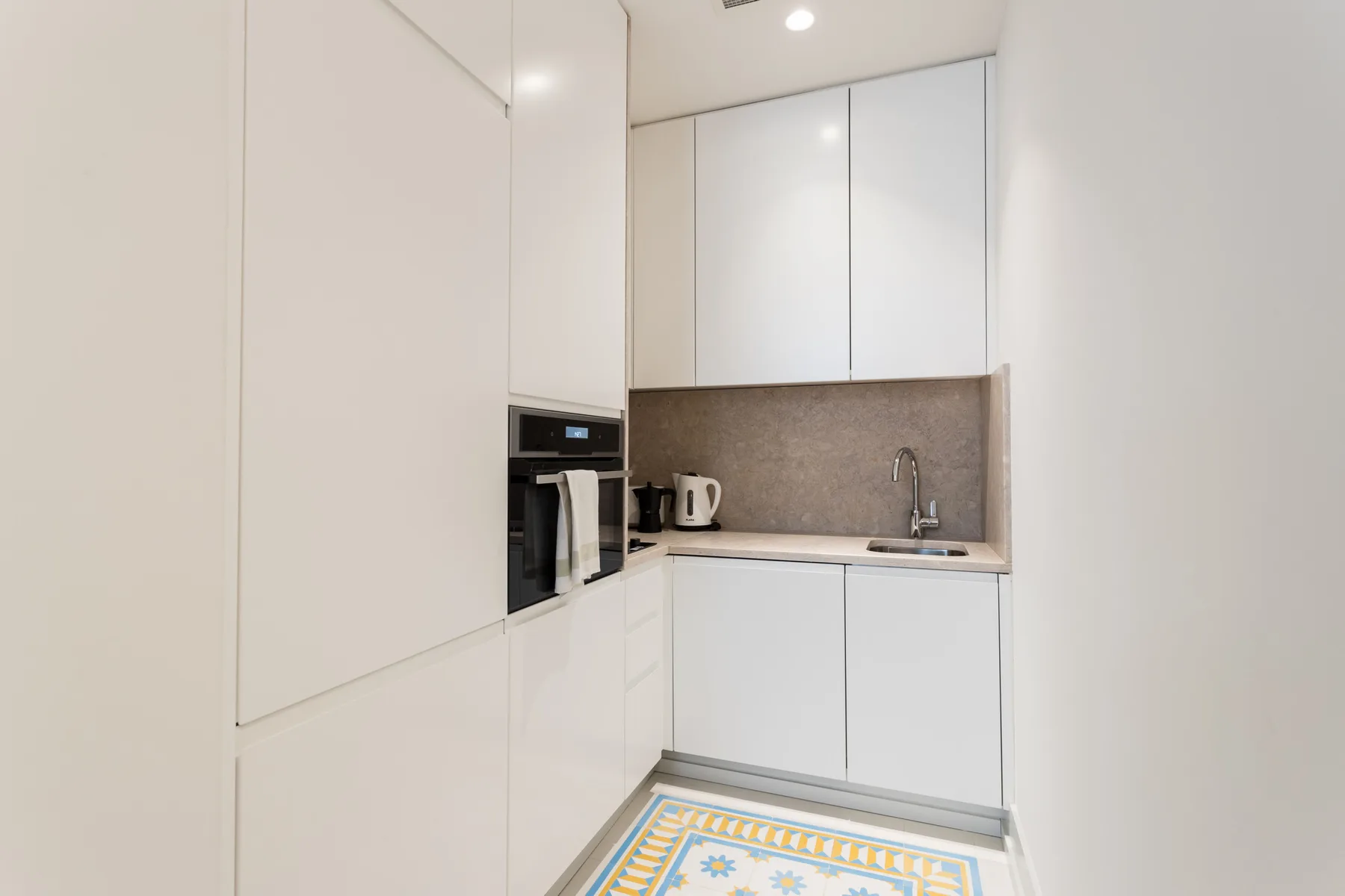 A compact white kitchen with built-in appliances and a patterned floor tile.