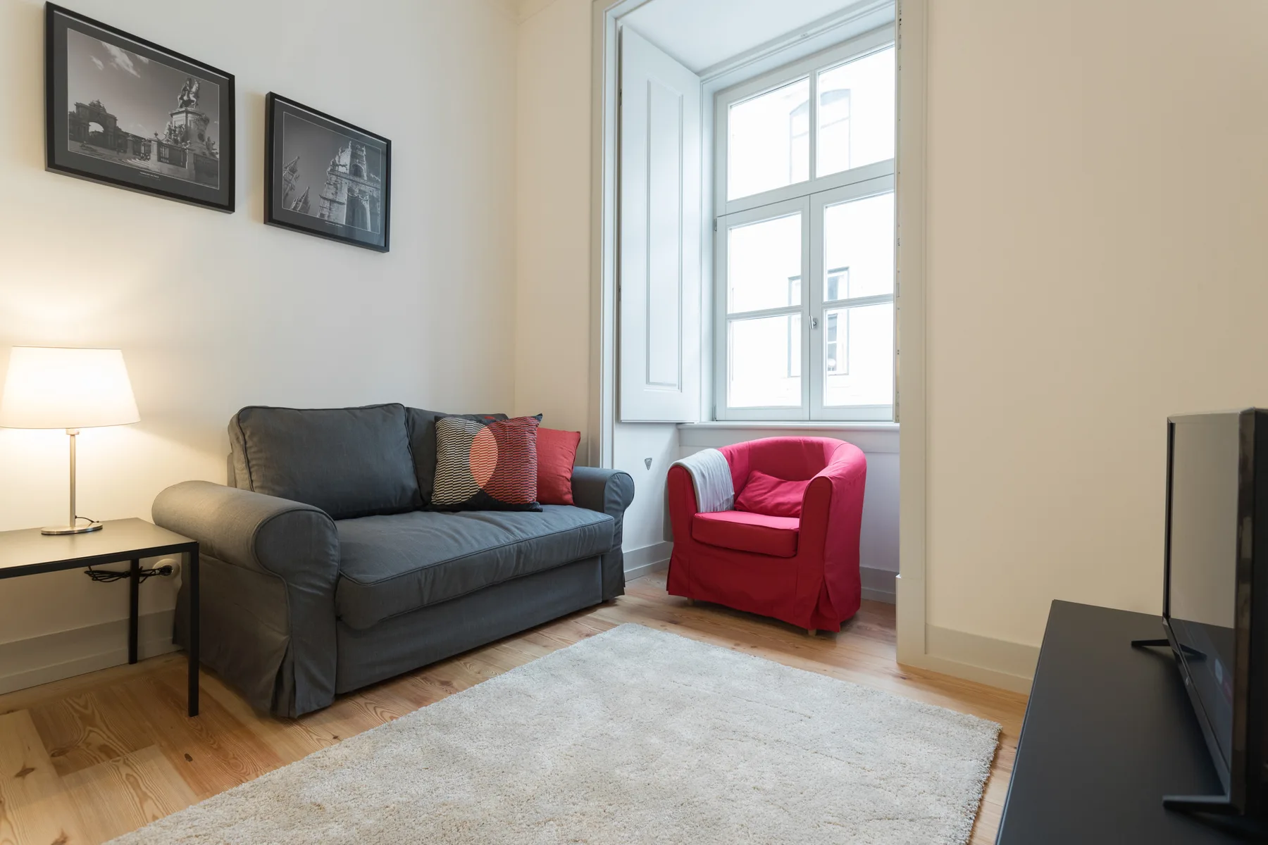 Living room with a gray sofa, red armchair, and large window.