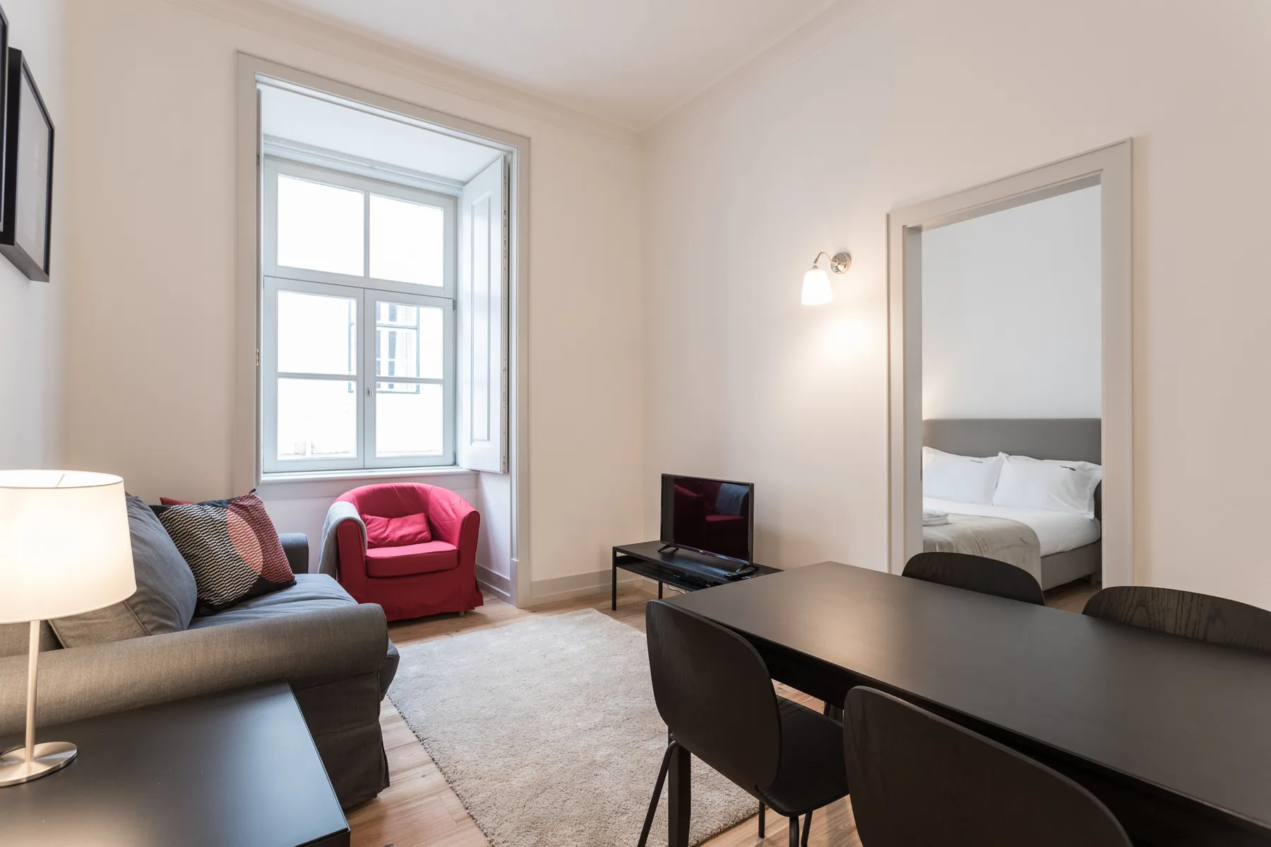 A bright living and dining area with seating, a television, and a bedroom doorway.