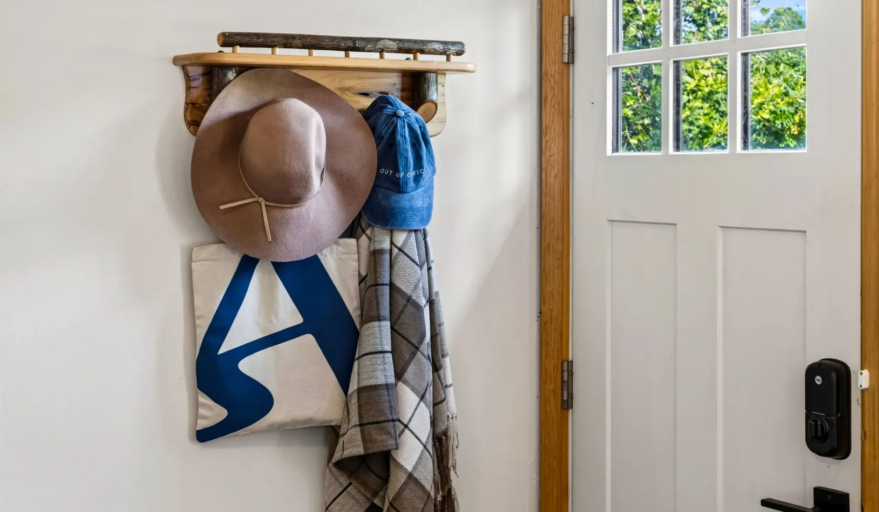 Una pared de entrada tiene un perchero de madera con sombreros y bolsos junto a una puerta.