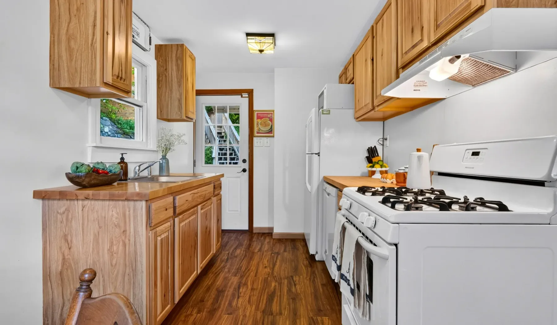 Una cocina con gabinetes de madera, encimeras y electrodomésticos blancos.