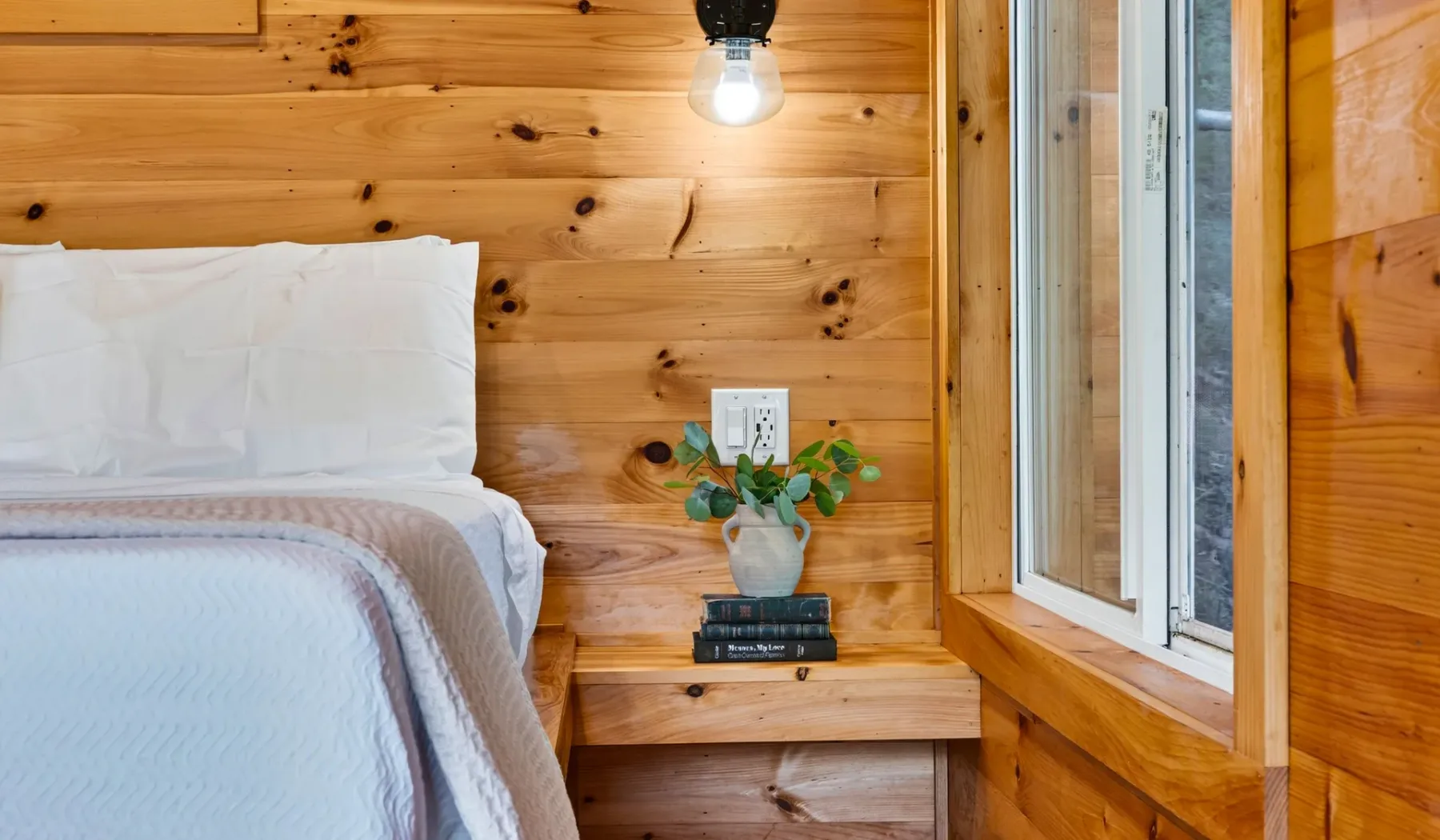 Un dormitorio con una cama bien tendida junto a una mesita de madera.