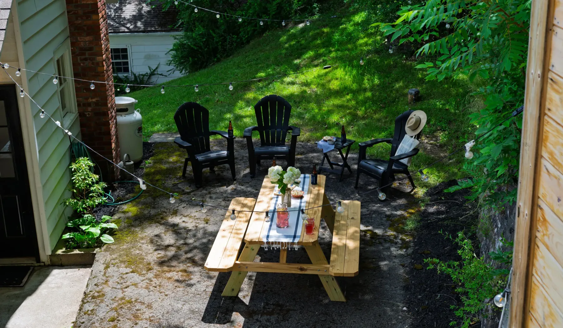 Una zona de estar al aire libre con una mesa de picnic de madera y luces colgantes.