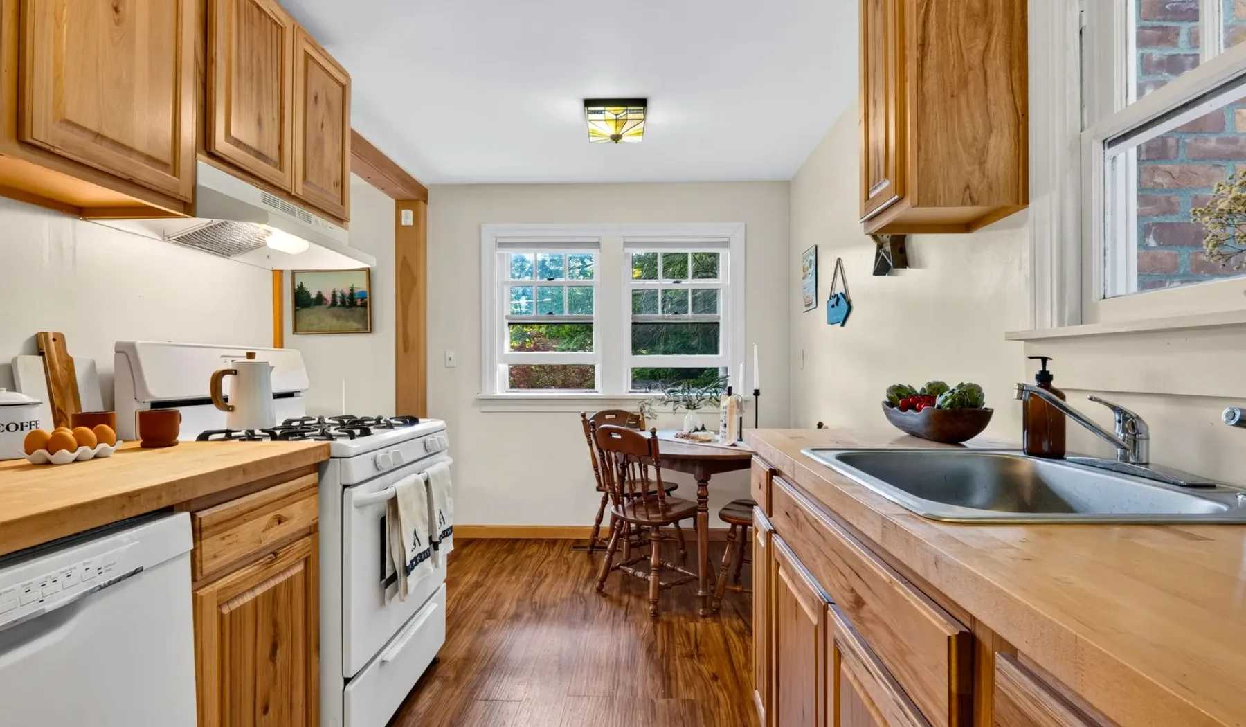 Una cocina luminosa con gabinetes de madera, encimeras y una mesa de comedor junto a las ventanas.