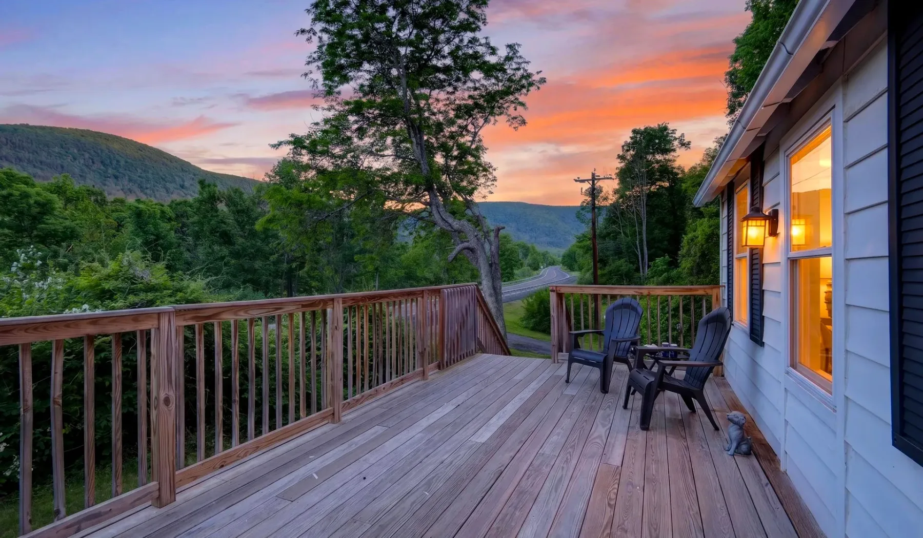 Una terraza de madera da a un valle boscoso bajo un cielo de atardecer colorido.