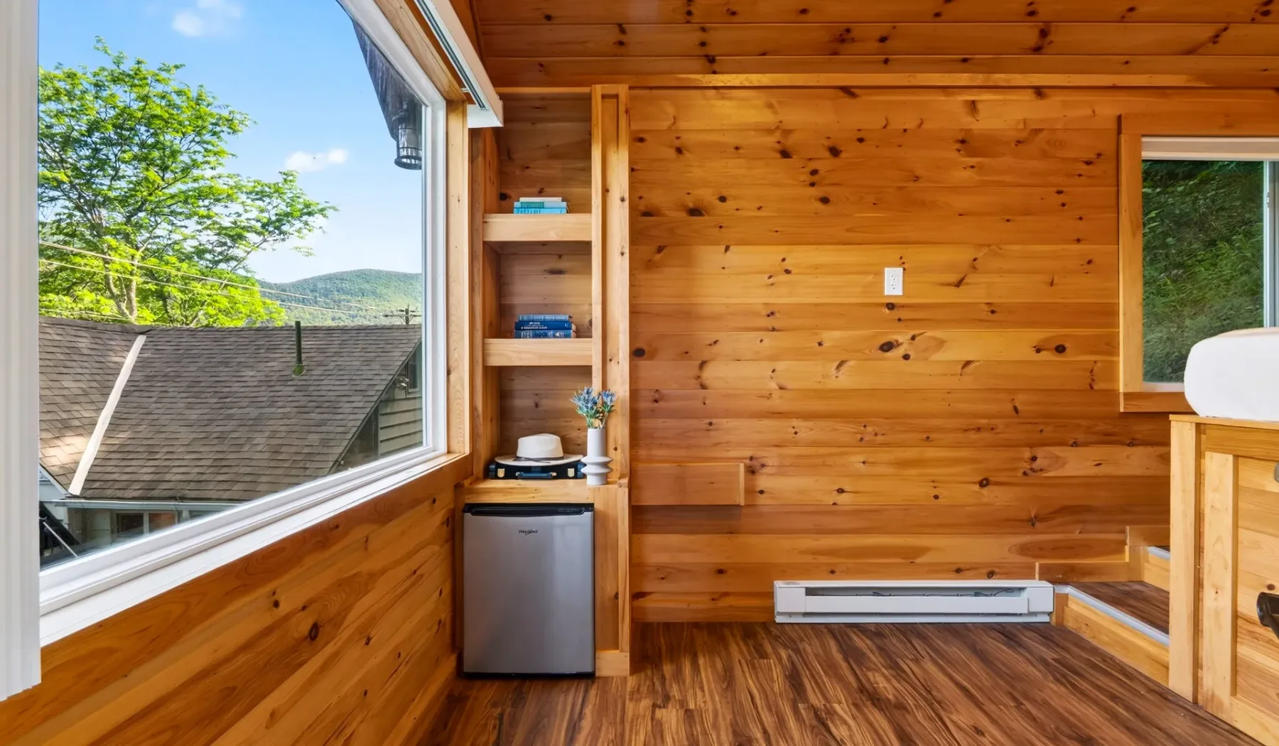 Una habitación revestida de madera con una ventana grande y un refrigerador compacto.