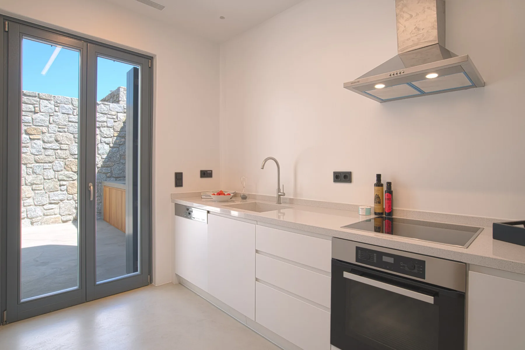 A bright modern kitchen with white cabinets, a cooktop, and an oven.
