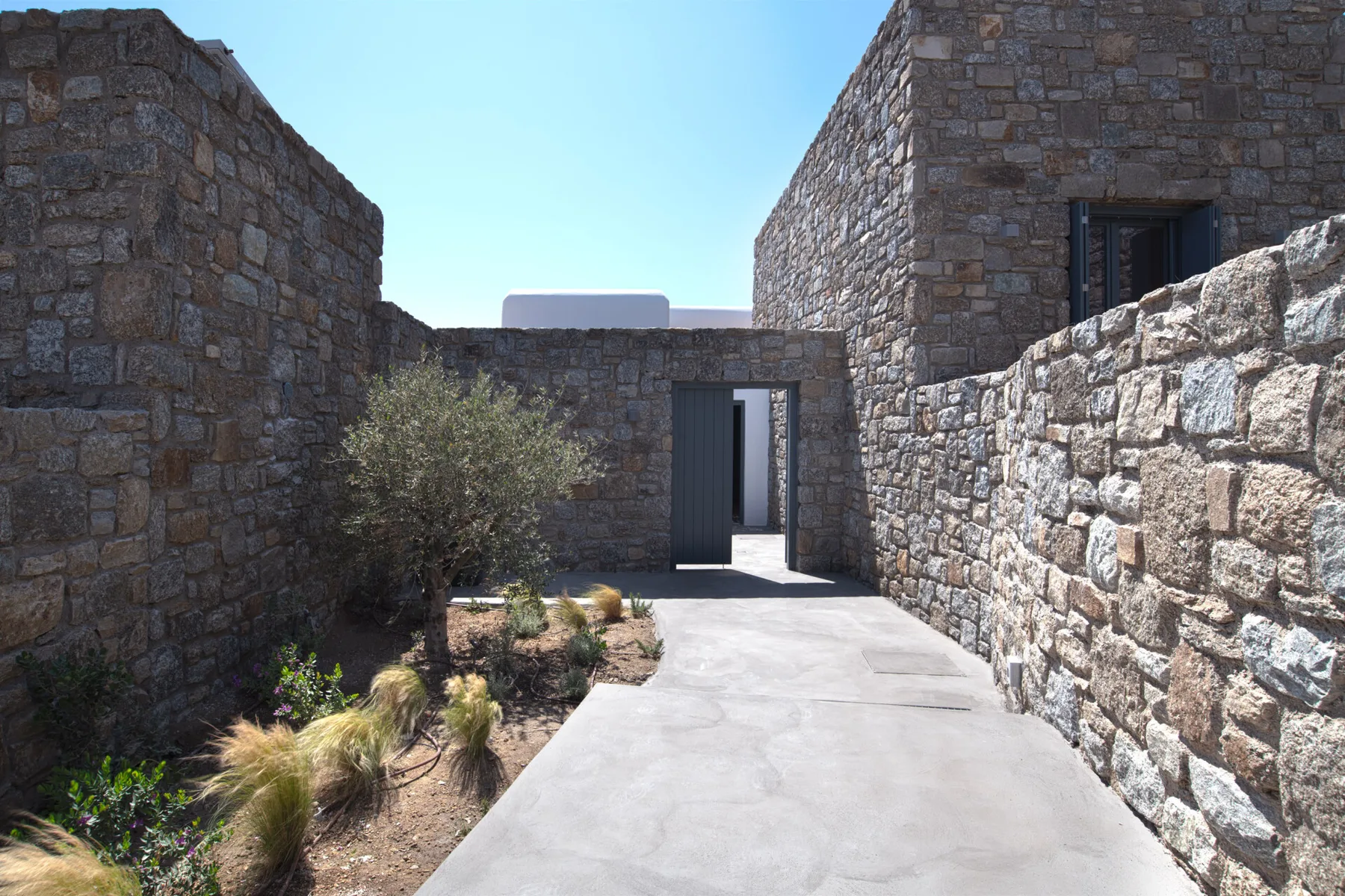 A paved walkway runs between stone walls toward an open doorway.