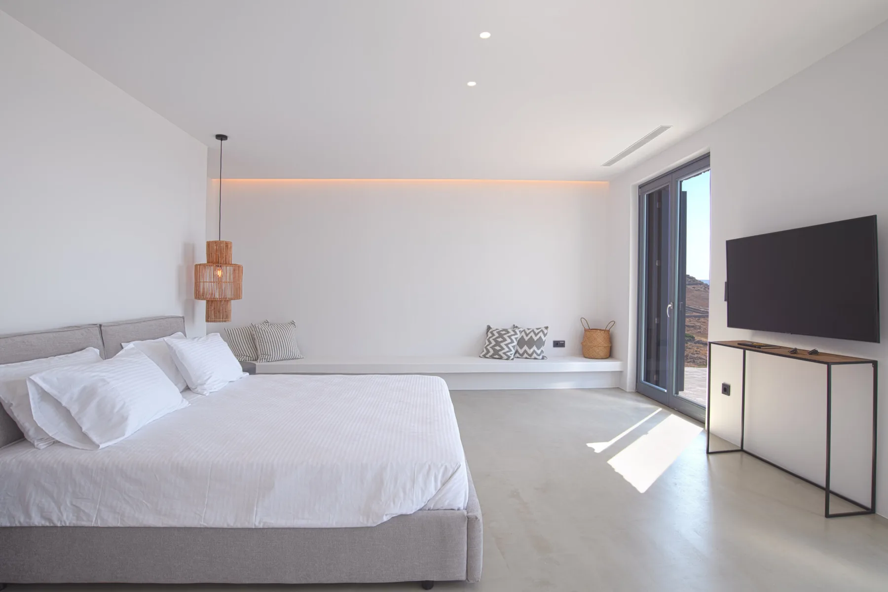 A bright bedroom with a bed, a television, and glass doors.