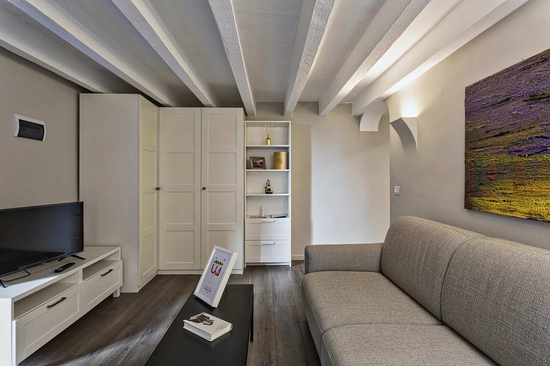 Una sala de estar con un sofá gris, un televisor y estanterías empotradas.